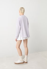 Felpa lavanda chiaro con vestibilità rilassata, collo rotondo e spalle basse, abbinata a una gonna bianca plissettata e sneaker bianche.