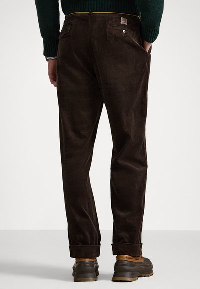 Barna bordás nadrág egyenes szabással és felgöngyölt szárakkal, hátsó zsebekkel és egy kis logócímkével a deréknál.