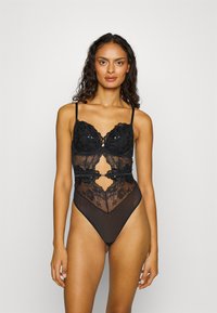 Body in pizzo nero con coppe imbottite, ricami floreali, pannelli in rete trasparente, spalline regolabili e design con gamba alta.