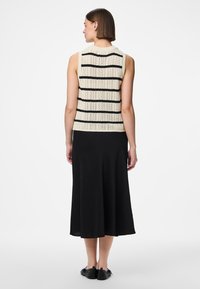 Μπλούζα χωρίς μανίκια σε κρεμ χρώμα με μαύρες οριζόντιες ρίγες, συνδυασμένη με μια μαύρη, ροή μίντι φούστα και μαύρες επίπεδες γόβες.