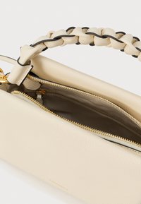 Borsa in pelle color crema con manico intrecciato, cerniera dorata e fodera interna in tessuto, parzialmente aperta che mostra il scomparto interno.