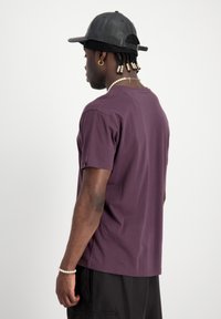 T-shirt violet à manches courtes en mélange de coton, coupe décontractée, avec un col rond et un détail d'emblème sur la manche gauche.