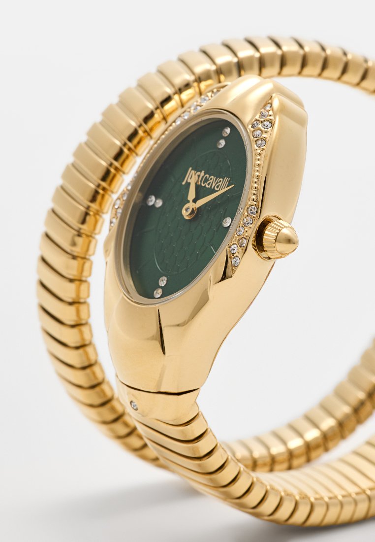Goudkleurig horloge met een gebogen groene wijzerplaat, bezet met kristallen. Heeft een flexibele band met een gladde, metalen afwerking.