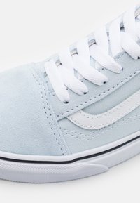 Baskets en daim bleu clair avec des lacets blancs, une empeigne texturée et une bande latérale blanche bordée de noir le long de la semelle.