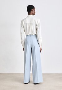 Blouse en crème claire avec un dos froncé, associée à un pantalon large bleu clair. Tissu lisse, coupe ajustée et taille mi-haute.