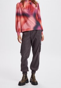 Långärmad tröja med ett rosa och grått gradientmönster, plisserad halsringning; i kombination med grå cargobyxor och kraftiga olivgröna ankelstövlar.