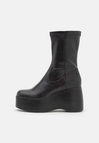 Bottes basses en cuir noir avec tige extensible, semelle plateforme et texture lisse. Caractérisées par un bout rond et un détail de couture minimaliste.