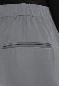 Pantalons gris avec une texture lisse, dotés d'une taille élastique et d'une seule poche passepoilée horizontale à l'arrière.