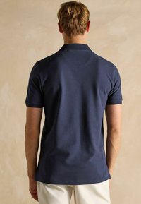 Merineer polo särk sujuvas puuvillases kangas, klassikalise kraega ja lühikeste varrukatega, millel on ühtlase seljaosa disain.