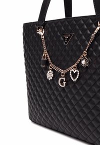Borsa a tote nera trapuntata con decorazioni in catena dorata che presenta charm decorativi, tra cui un lucchetto e lettere, texture liscia.