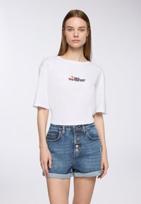 Biała koszulka z krótkim rękawem z graficznym napisem "NOWA WIADOMOŚĆ DLA CIEBIE" oraz wzorem z wisienką. W połączeniu z niebieskimi szortami dżinsowymi z przodem na guziki.