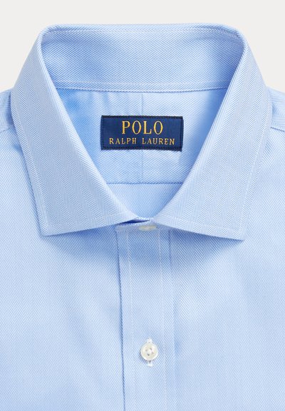 Vaaleansininen puku- / kauluspaita kalanruotokuvioinnilla, valkoinen nappi ja laivastonsininen Polo Ralph Lauren -etiketti kauluksen sisäpuolella.
