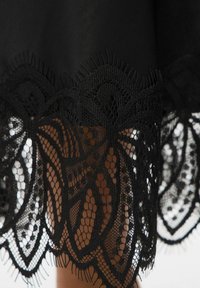 Zwarte stoffen rok met een ingewikkelde kanten rand aan de zoom, met een bloemenpatroon met delicate details en een gelaagde textuur.