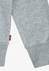 Tejido de sudadera gris con puños acanalados. Presenta una etiqueta roja con la inscripción "Levi's" en la costura lateral, destacando una textura suave y lisa.