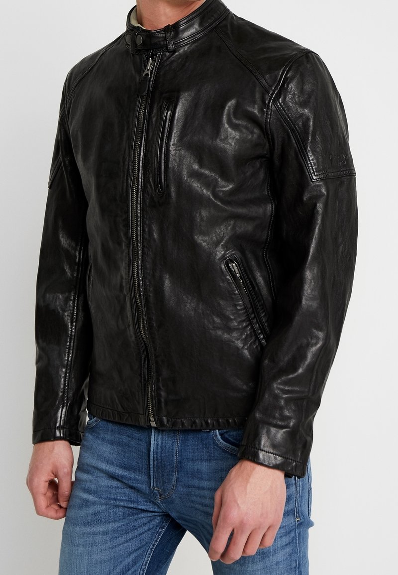 Svart läderjacka med ståkrage, främre dragkedja och sidofickor. Har sömlösa axlar och en figurnära design för en elegant look.