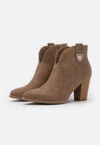 Brune ankelstøvler i imiteret ruskind med spids tå, lynlåse i siden og en stakket træhæl. Har udskæringsdetaljer og dekorative beslag.