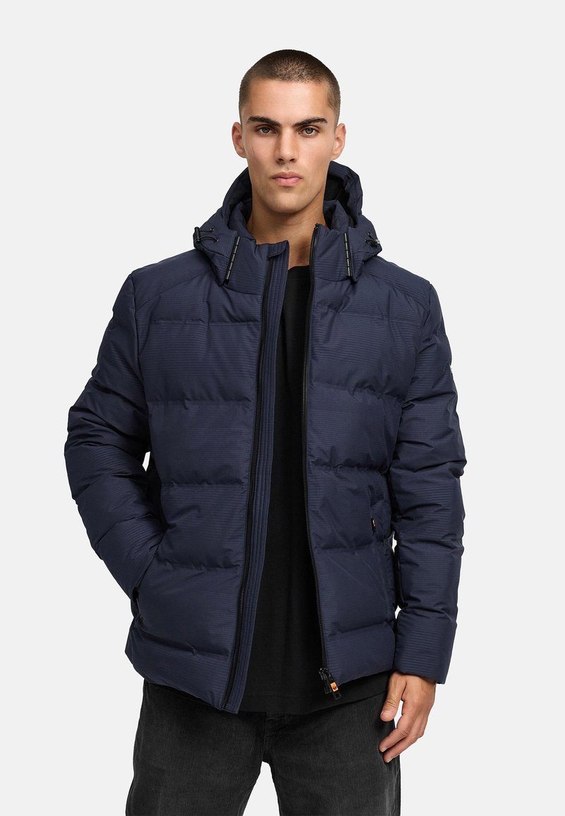 Marineblå pufferjacka med dragkedja fram, hög krage och justerbar huva. Texturerat tyg med quiltat mönster, hållbara dragkedjor och sidfickor.