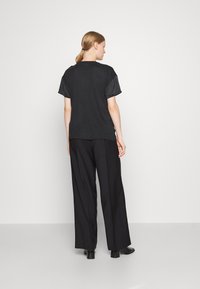 Schwarzes T-Shirt mit kurzen Ärmeln, glatter Stoff, lässige Passform. Kombiniert mit weit geschnittenen schwarzen Hosen und Ankle-Boots, vor einem schlichten Hintergrund.