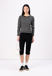 Svart och vit randig långärmad topp kombinerad med svarta bermuda-shorts. Skorna är svarta joggingskor med vita detaljer. Vit handväska.