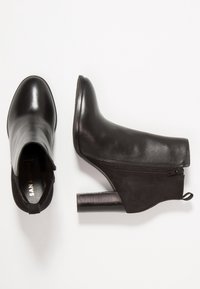 Botas de cuero negro hasta el tobillo con puntera redonda, cremallera lateral y tacón bloque texturizado. Acabado suave y una lengüeta en la parte posterior.