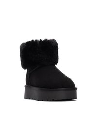 Botín negro de ante con un suave puño de pelaje sintético y una gruesa suela de goma negra, con una punta redondeada y costuras visibles.