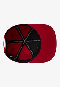 Red cap with a black interior, flat brim, and ventilation holes. Features printed text inside and a logo accent at the back.