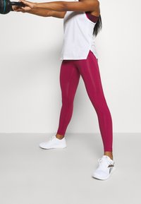 Slimmade, högmidjade leggings i livlig magenta med en slät, elastisk textur. Matchat med en lös vit tanktop och vita träningsskor.