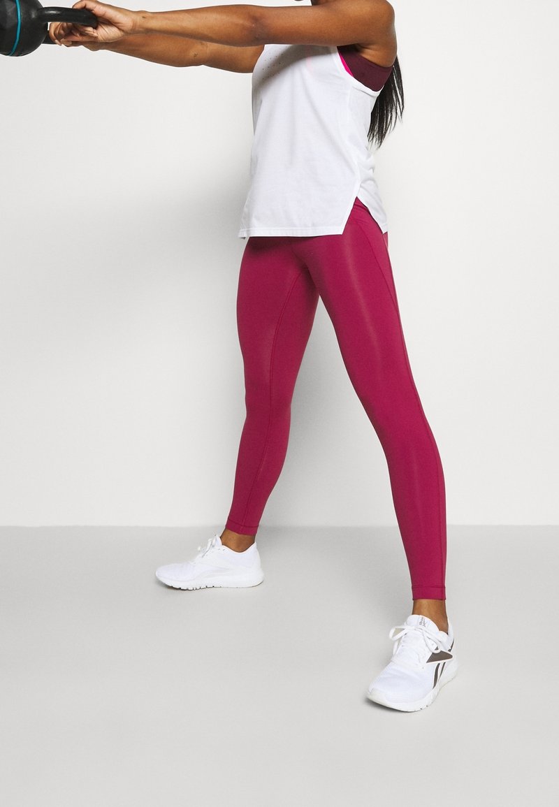 Slimmade, högmidjade leggings i livlig magenta med en slät, elastisk textur. Matchat med en lös vit tanktop och vita träningsskor.