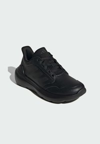 Scarpe da ginnastica nere in pelle sintetica con suola curva, caratterizzate da pannelli testurizzati e chiusura con lacci. Design semplice con accenti minimi.