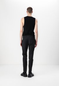 Svart ärmlös topp tillsammans med skräddarsydda svarta byxor och svarta snörskor, med en ren och minimalistisk design.