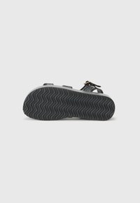 Svart sandal med suede-overdel, justerbare stropper og gullhardware. Teksturert gummisåle med bølgete mønster for grep og komfort.