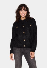 Svart, texturerad cardigan med guldknappar, två bröstfickor och rund halslinning. Bärs över mörkgrå jeans, långärmad, avslappnad passform.