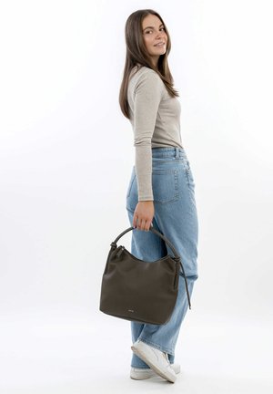 Dark green leather handbag with a soft, textured finish and a curved top handle, shown being held by a person wearing light jeans and a beige top.