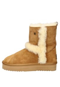 Bruine suède enkelboot met een zachte crèmekleurige schapenvachtvoering, platte rubberen zool en decoratieve knoopdetails aan de zijkant.