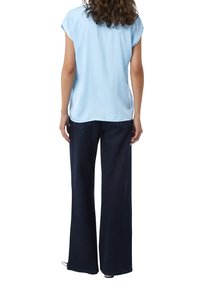 Helles blaues kurzärmliges Blusenshirt mit lässiger Passform, kombiniert mit dunkelblauen weit geschnittenen Jeans mit Taschen und geradem Saum.
