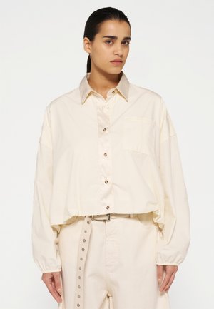 Lichtbeige knop-up shirt met een kraag, oversized pasvorm en een borstzak. Zachte katoenen stof met een subtiele glans.