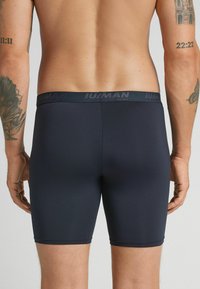 Mörkblå boxerkalsonger med en slät yta, som har ett subtilt loggat midjeband och en figursydd design som sträcker sig till mitten av låret.