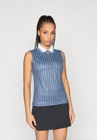 Ujjatlan póló kék színben, geometrikus mintával, fehér gallérral és cipzáras záródással. A modellen fekete szoknya van.