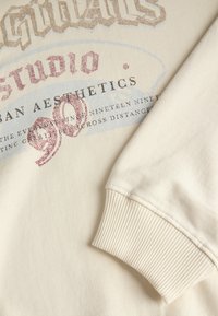 Felpa off-white con stampa grafica frontale e testo multicolore, polsini a costine e una texture di tessuto liscia.