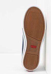 Niebieska podeszwa sneakerów Levi's ma brązową gumową bazę z wzorem jodełkowym, białą środkową podeszwę i czerwone logo Levi's.