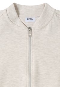 Veste beige clair à fermeture éclair argentée avec une étiquette de marque "CECIL" au col, fabriquée en tissu doux chiné.