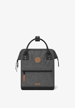 Gray fabric backpack with black leather accents, round logo patch, top handle, front zip pocket, and two side pockets. Rectangular shape.