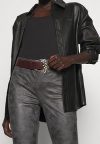 Svart lädertröja, figurnära svart linne, grå texturerade byxor, och ett vinrött bälte med en dekorativ silverknäppning.