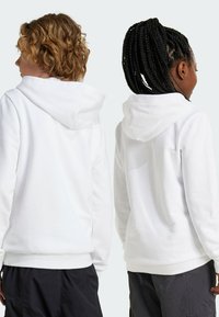 Felpe bianche con cappuccio, dal tocco morbido, cuciture laterali e polsini a costine; indossate da due persone, una con i capelli ricci e l'altra con le trecce.