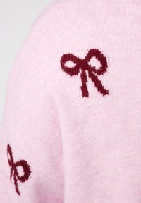 Zacht roze gebreide stof met kleine donkerrode strikontwerpen geborduurd vlakbij de schouder en het armgebied.