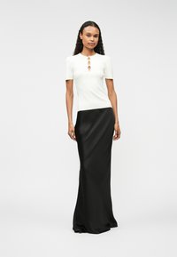 Biała krótka bluzka z okrągłym dekoltem i złotymi akcentami, zestawiona z czarną satynową spódnicą do ziemi, o gładkiej teksturze.