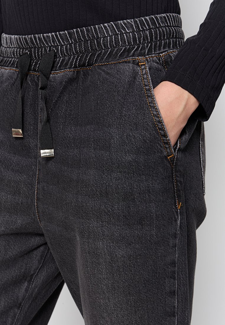 Joggers in denim nero con vita elastica, cordoncino, tasche laterali e dettagli di cucitura arancioni a contrasto. Tessuto a trama piatta.