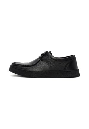 Zapato de cuero negro con una superficie texturizada, punta redonda y diseño de cordones. Presenta una suela gruesa de goma y acentos minimalistas.