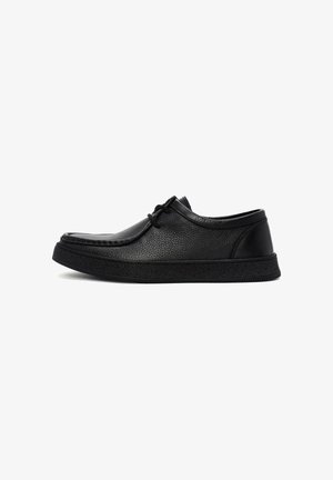 Black leather shoe with a textured surface, round toe, and lace-up design. Features a thick, rubber sole and minimalistic accents.