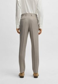 Pantaloni beige su misura con una texture liscia, dotati di tasche posteriori e un design a gamba dritta. Indossati con una camicia di colore chiaro.